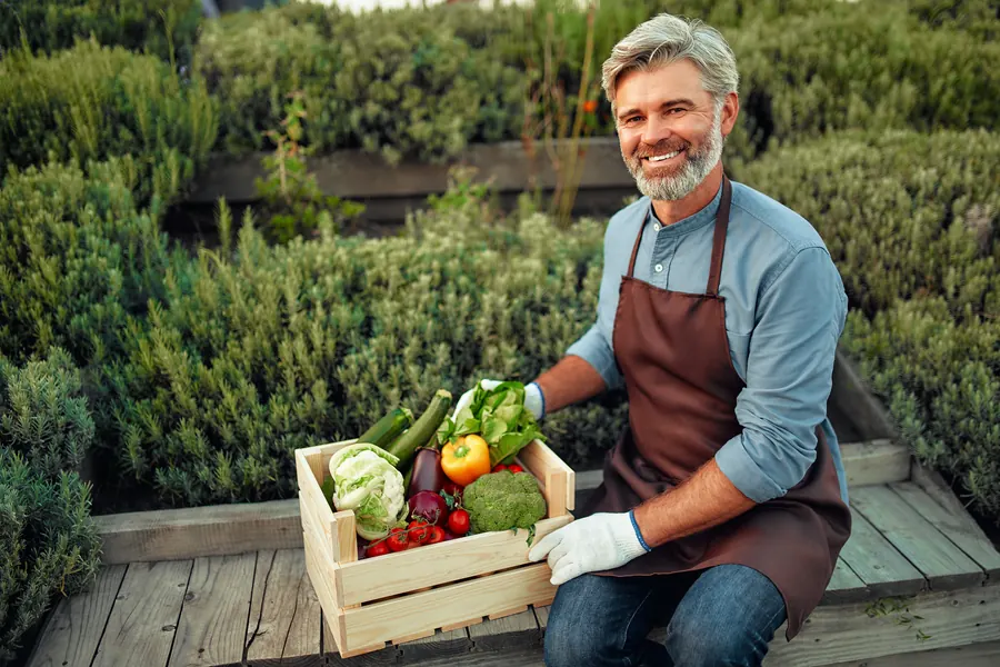 Un maraîcher souriant avec sa récolte de légumes