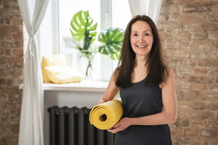 Une professeure de yoga, tapis sous le bras, dans une salle lumineuse